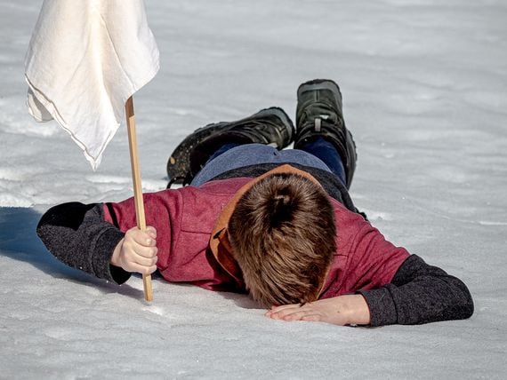 Boy lying down in snow waving the white flag of surrender (Jackson Simmer/Unsplash)