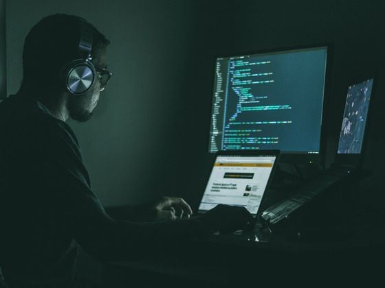 CDCROP: Man wearing headphones sits at computer coding (Unsplash)