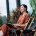 Contemplated young Asian woman looking away in thought while relaxing on deck chair using laptop in the backyard, surrounded by beautiful houseplants. Lifestyle and technology