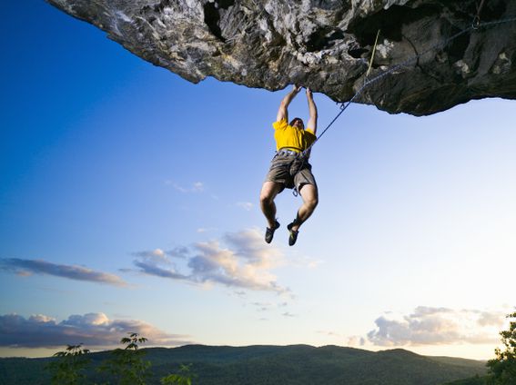 Male rock climber clinging to overhanging rock, low angle view