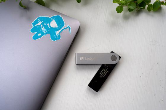 Photo of a Ledger USB drive with the corner of a laptop peaking on the left side of the frame.