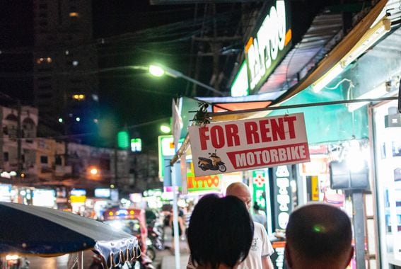 A sign reading "For Rent: Motorbike" hangs above a neon-lit street.