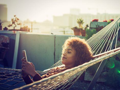 Young woman checks smartphone from hammock