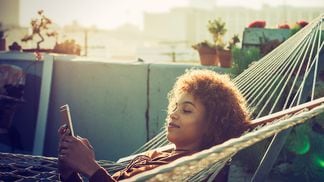 Young woman checks smartphone from hammock