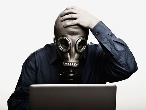 Shot of man in front of laptop wearing gas mask (Getty)