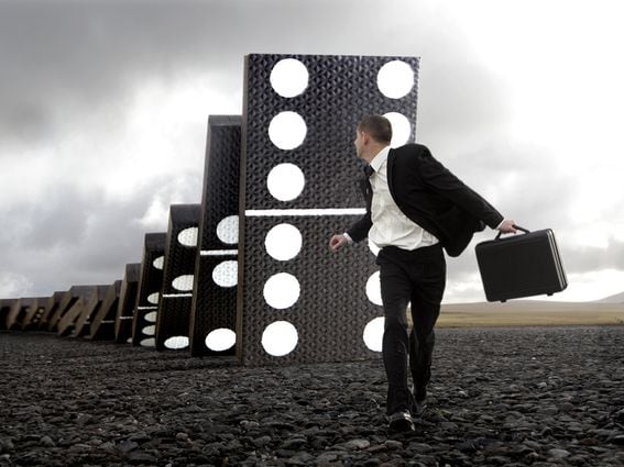 CDCROP: Male executive running from giant falling dominoes (Getty Images)
