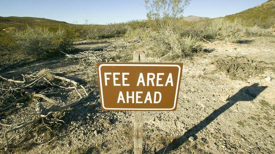 Sign saying fee area ahead on a background of desert shrubland