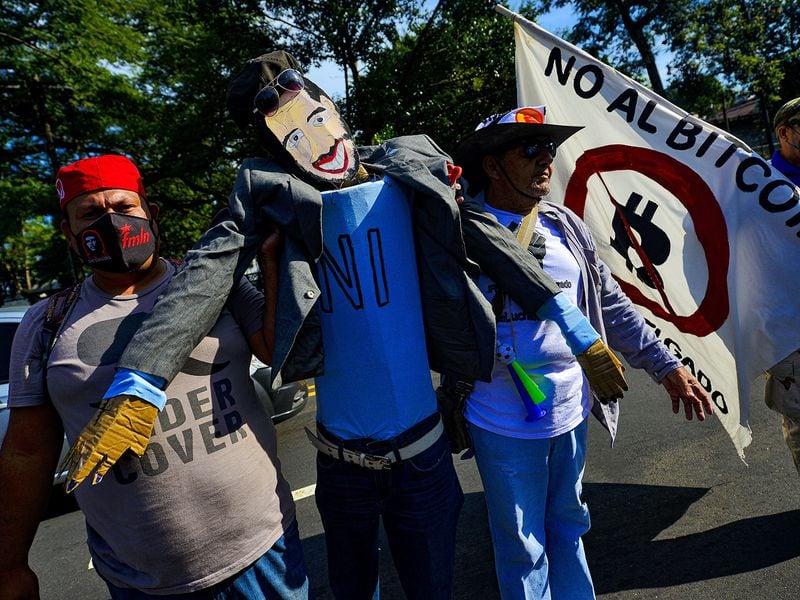 SAN SALVADOR, EL SALVADOR - OCTOBER 17: A demonstrator holds an effigy of President Nayib Bukele next to a sign against the approved Bitcoin law during a protest against the government on October 17, 2021 in San Salvador, El Salvador. (Photo by Emerson Flores/APHOTOGRAFIA/Getty Images)