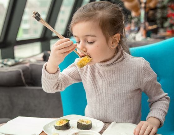 Charming funny girl eating sushi in a restaurant
