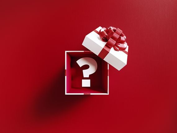Question mark is coming out of a white gift box tied with red ribbon on red background. Horizontal composition with copy space. Directly above. Great use for Christmas related gift concepts.