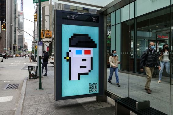 NEW YORK, NEW YORK - MAY 11: People wearing protective masks walk past a CryptoPunk digital art non-fungible token (NFT) displayed on an electronic billboard at a bus shelter in Midtown Manhattan on May 11, 2021 in New York City. The image is part of SaveArtSpace's "Pixelated" public art exhibition which will be displaying 193 of Larva Labs' CryptoPunks on phone booths, bus shelters, and billboards around New York City during the month of May. (Photo by Dia Dipasupil/Getty Images)