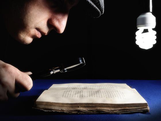 Man looking to an old book through magnifying glass