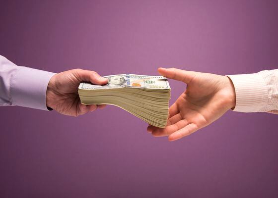 One man and one woman's hands handing off large stack of US 100 bills, purple background