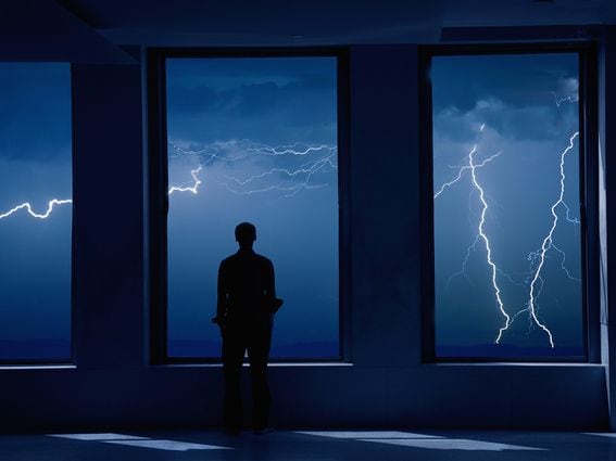 Man staring out window at lightning storm (Grant Faint/Getty Images)