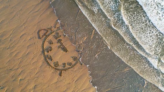 Clock drawn in sand at water's edge