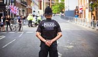A U.K. policeman seen from behind stands in the middle of road