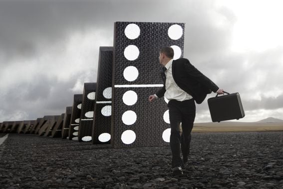 Male executive running from giant falling dominoes