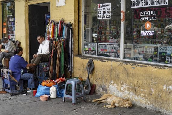 Photo of a person shining a man's shoes in El Salvador on the sidewalk and a dog sleeping.