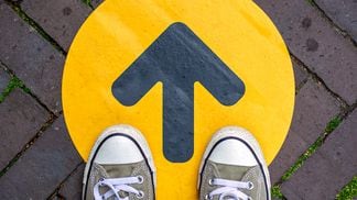 CDCROP: Feet wearing sneakers in front of arrow on road outdoors. Direction arrow in front of a store for the social distancing during the covid-19 pandemic. (Getty Images)