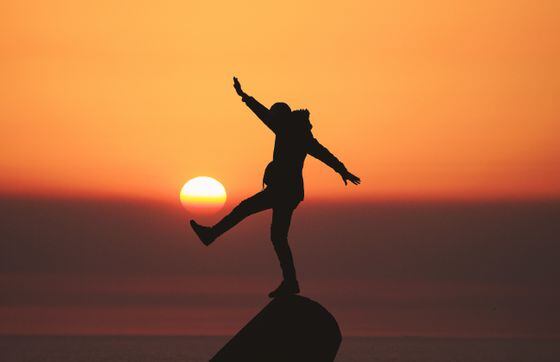 a man balancing on a rock with an orange sunset in the background, representing bitcoin as an equalizer