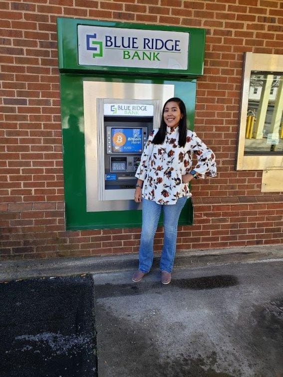 Blue Ridge Bank employee poses with one of the bank's ATMs, now equipped to offer bitcoin services.