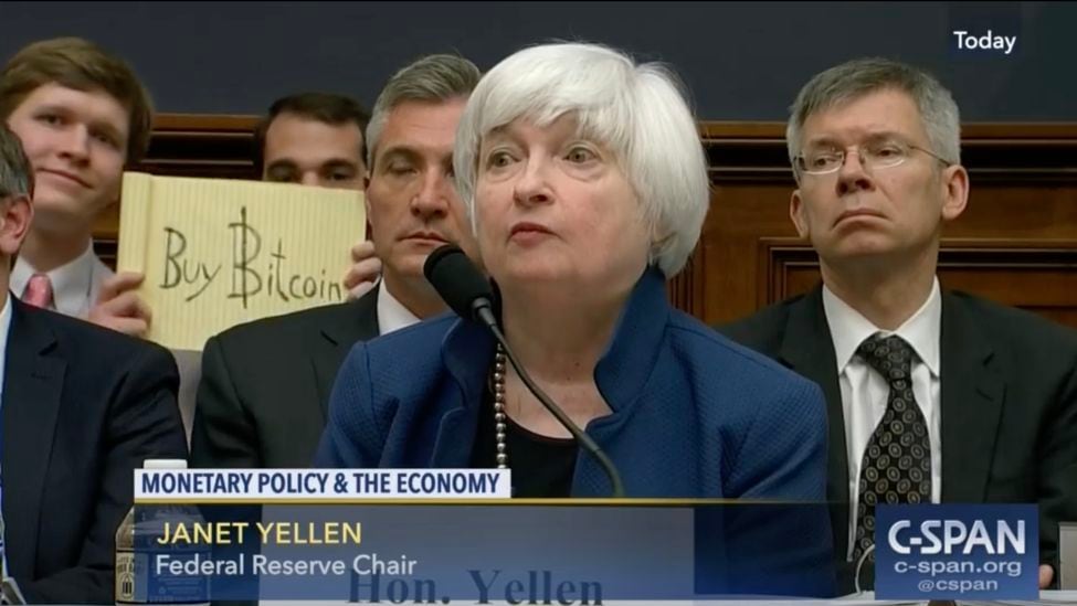 2017 年 7 月，在众议院金融服务委员会听证会上，克里斯蒂安·朗格莱斯 (Christian Langlais) 在美联储主席珍妮特·耶伦 (Janet Yellen) 身后举着“购买比特币”的标语。（C-Span）