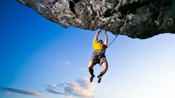 Male rock climber clinging to overhanging rock, low angle view