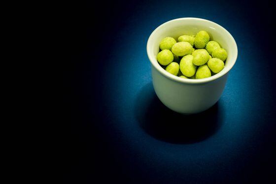 Green wasabi nuts in a cup on a dark background.