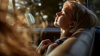 Woman with headphones relaxing in car, at sunset